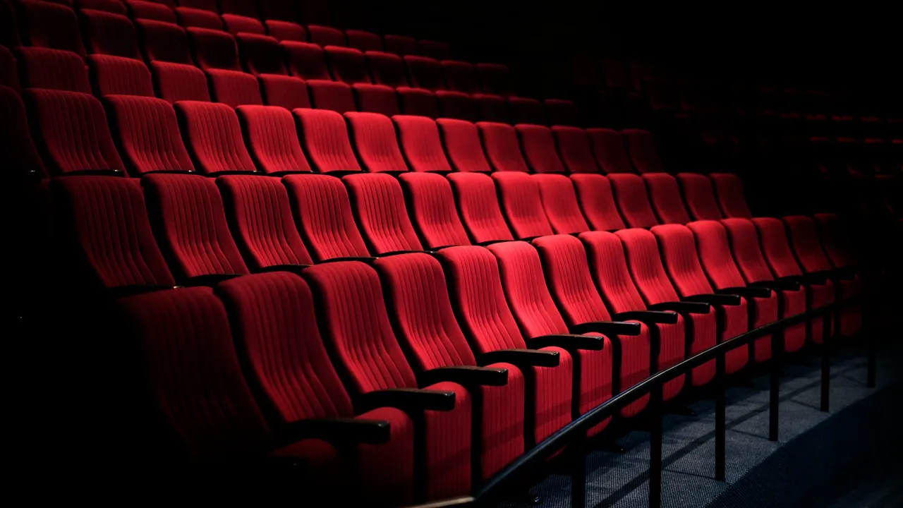 Fileiras de poltronas vermelhas em uma sala de teatro
