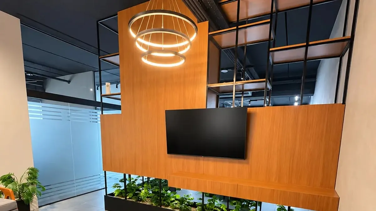 Recepção do escritório com painel de madeira, TV, luminária circular e jardim interno